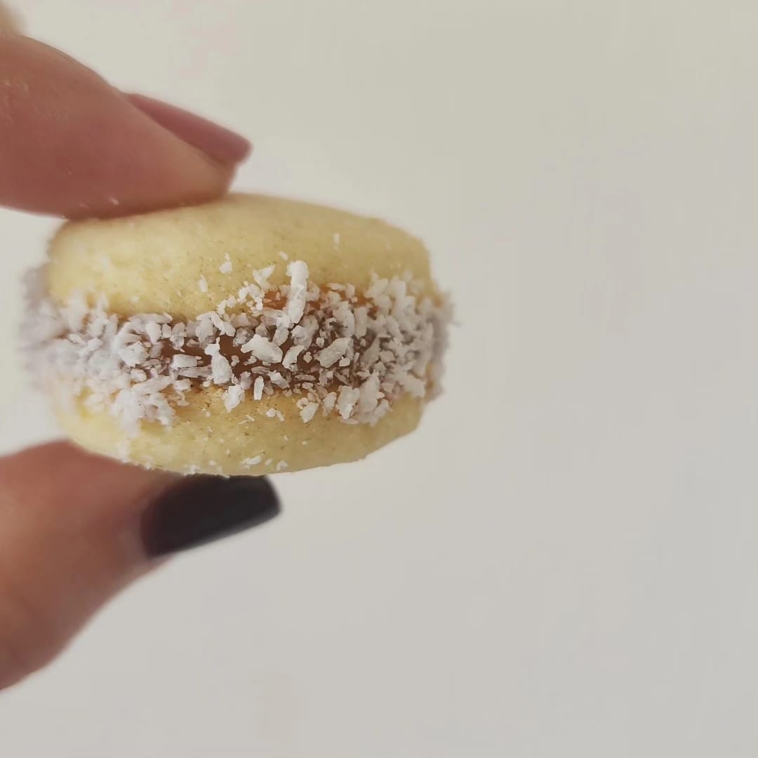 Alfajor de manjar bañado en coco rallado, sostenido en la mano